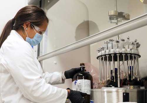 student in lab coat working under a fume hood
