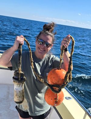 grad student standing at the rear of a boar holding a deviceattached to an orange bouy