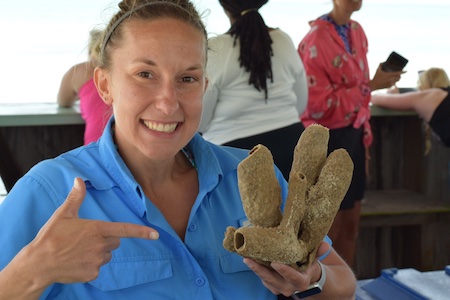 Dr. Molly Miller photo of Molly pointing to a large piece of coral in her hand
