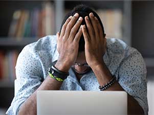 Man holding head in hands leaning on desk.